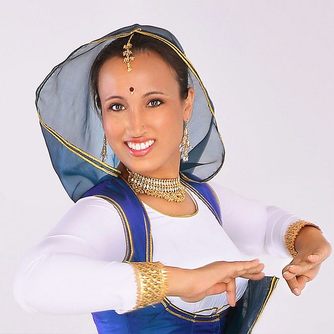 A woman in blue and white dress pointing to her face.