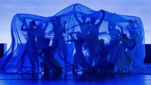 A group of people dancing in front of a blue background.